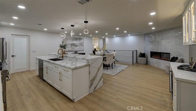 kitchen with sink, an island with sink, white cabinetry, and light hardwood / wood-style floors