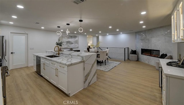 kitchen with white cabinets, light stone countertops, a kitchen island with sink, a fireplace, and a sink