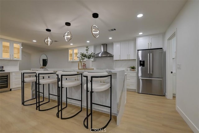 kitchen featuring white cabinetry, light countertops, stainless steel fridge with ice dispenser, wall chimney exhaust hood, and glass insert cabinets