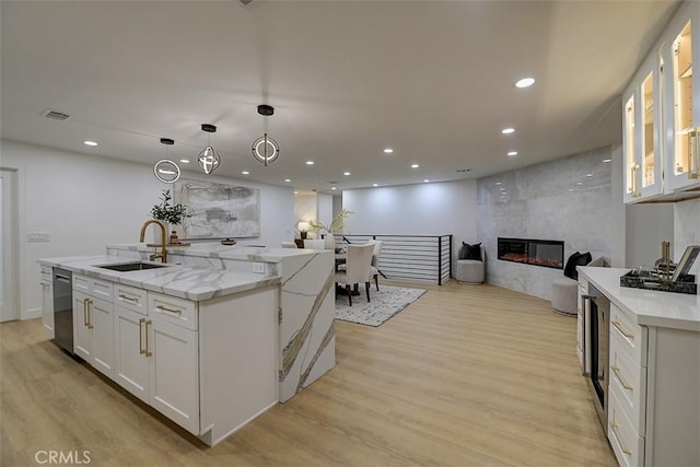 kitchen with light stone counters, white cabinetry, a sink, and an island with sink