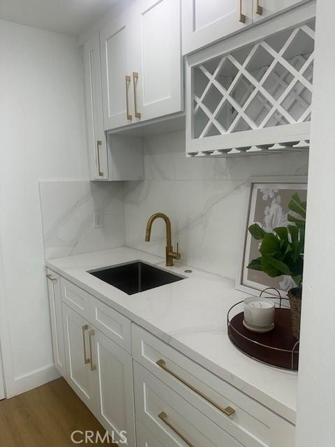 kitchen with a sink, white cabinetry, baseboards, decorative backsplash, and dark wood finished floors