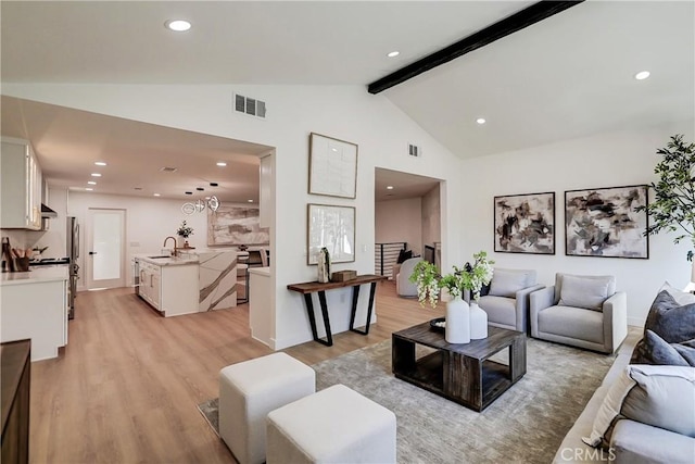 living room with light hardwood / wood-style floors, sink, high vaulted ceiling, and beam ceiling