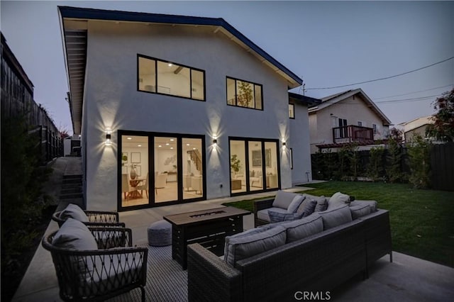 back of house at dusk with a patio, fence, a lawn, stucco siding, and an outdoor living space with a fire pit