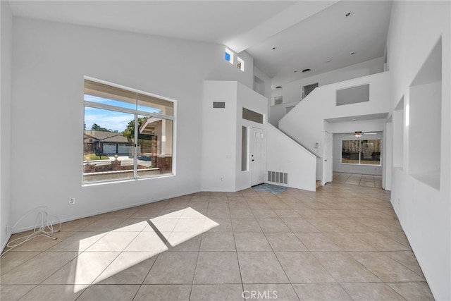 unfurnished living room featuring light tile patterned floors, a towering ceiling, and ceiling fan