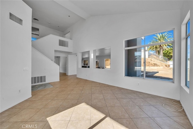 unfurnished living room with beam ceiling, light tile patterned floors, and high vaulted ceiling