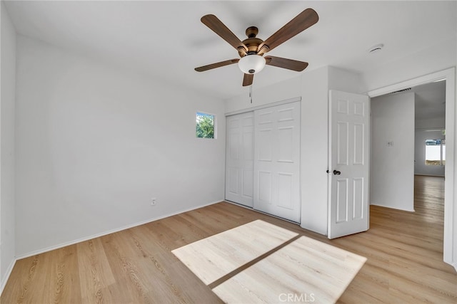 unfurnished bedroom featuring ceiling fan, light wood-type flooring, multiple windows, and a closet