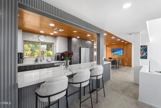 kitchen with white cabinetry, sink, light stone counters, and a kitchen bar