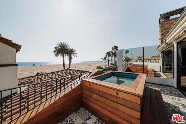 exterior space featuring an outdoor hot tub, a balcony, and a water view