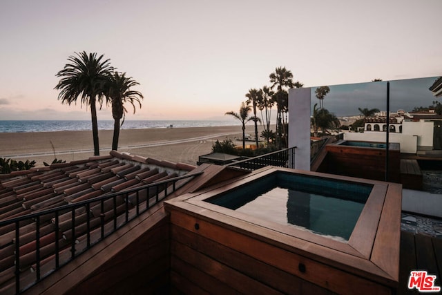 pool at dusk with an in ground hot tub and a water view