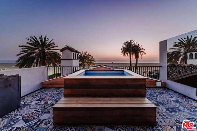 deck at dusk with a patio area, a hot tub, and a water view