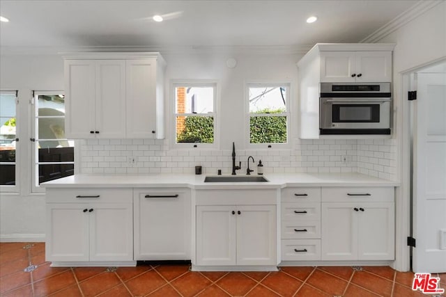 kitchen featuring sink, stainless steel oven, tile patterned flooring, decorative backsplash, and white cabinets