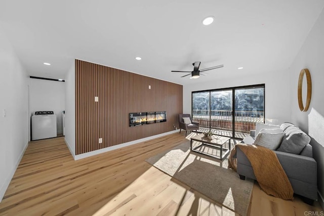 living room with washer / clothes dryer, ceiling fan, light hardwood / wood-style floors, and wood walls