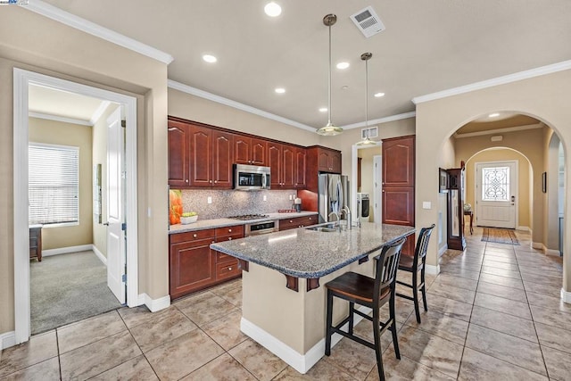 kitchen featuring light carpet, a center island with sink, a breakfast bar area, stainless steel appliances, and hanging light fixtures