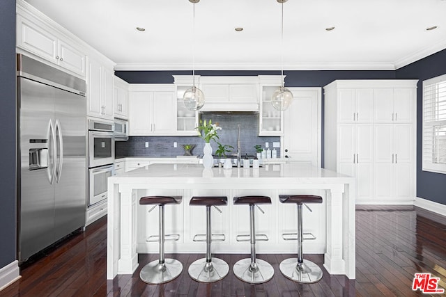 kitchen with pendant lighting, built in appliances, a kitchen breakfast bar, and an island with sink