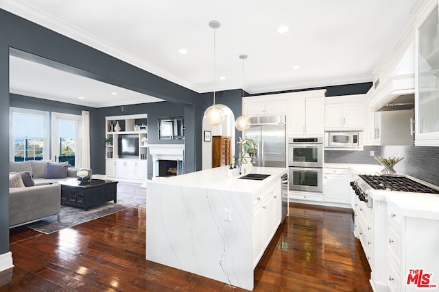 kitchen featuring white cabinetry, decorative backsplash, built in appliances, pendant lighting, and a kitchen island with sink