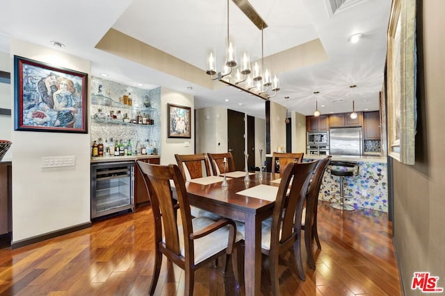 dining room with a raised ceiling, beverage cooler, dark wood-type flooring, an inviting chandelier, and bar area