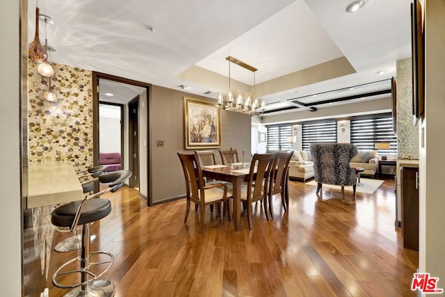 dining room with hardwood / wood-style floors, a raised ceiling, and a chandelier