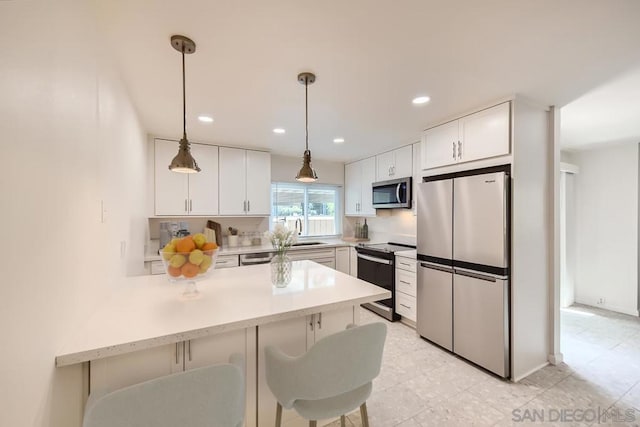 kitchen featuring kitchen peninsula, appliances with stainless steel finishes, white cabinetry, hanging light fixtures, and a breakfast bar area