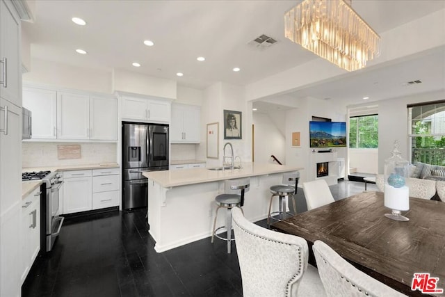 kitchen featuring dark hardwood / wood-style flooring, a kitchen island with sink, a breakfast bar, white cabinets, and appliances with stainless steel finishes