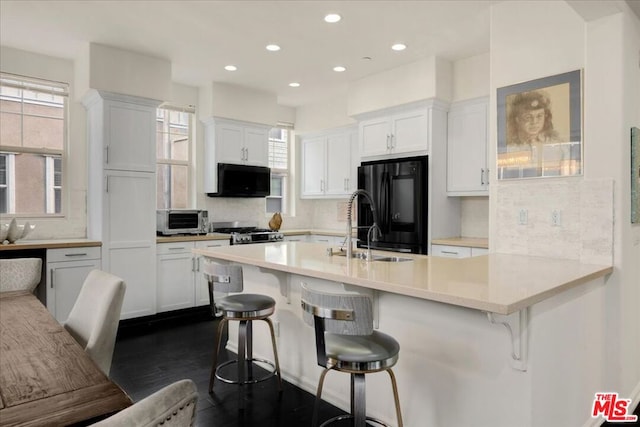 kitchen featuring a kitchen bar, stove, white cabinetry, and black fridge