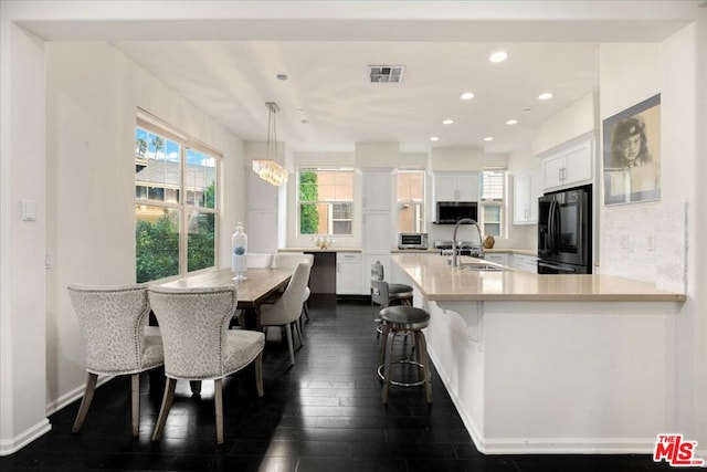 kitchen with white cabinetry, sink, a kitchen breakfast bar, black fridge, and decorative light fixtures