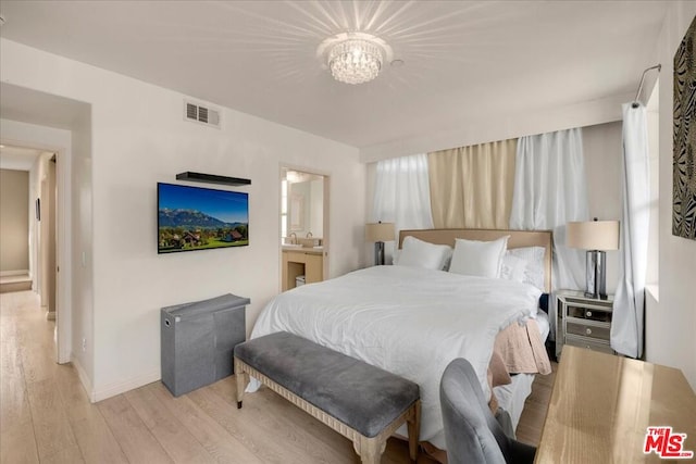 bedroom featuring connected bathroom, light hardwood / wood-style flooring, and an inviting chandelier