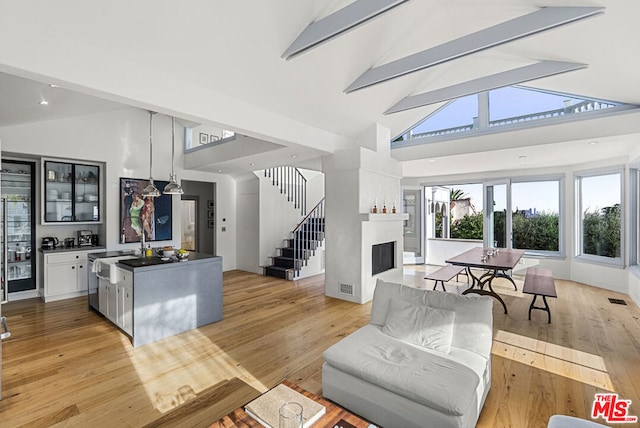 living room featuring beam ceiling, light wood-type flooring, high vaulted ceiling, and sink