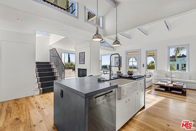 kitchen featuring white cabinetry, beamed ceiling, stainless steel dishwasher, pendant lighting, and a kitchen island with sink