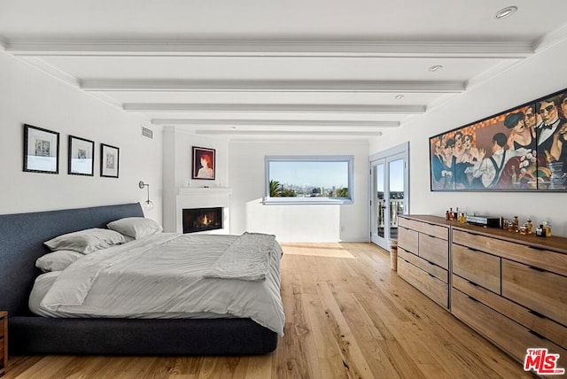 bedroom with beamed ceiling, french doors, a large fireplace, and light hardwood / wood-style flooring