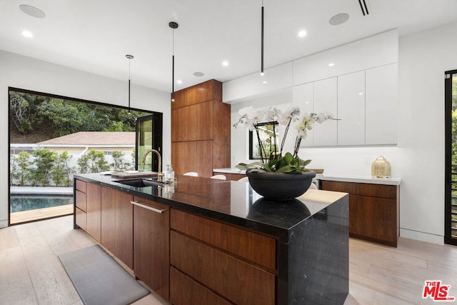 kitchen featuring pendant lighting, white cabinets, sink, light hardwood / wood-style flooring, and a large island