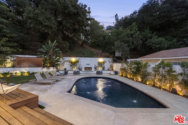 pool at dusk featuring pool water feature, a patio, and an outdoor fireplace