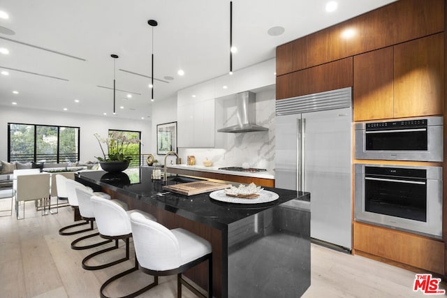 kitchen featuring appliances with stainless steel finishes, a spacious island, wall chimney range hood, pendant lighting, and white cabinets