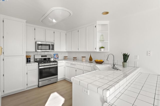 kitchen featuring stainless steel appliances, kitchen peninsula, tile countertops, sink, and white cabinetry