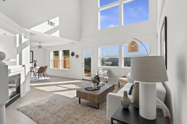 living room with ceiling fan, light hardwood / wood-style flooring, and a towering ceiling