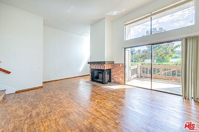 unfurnished living room with a fireplace, a towering ceiling, a textured ceiling, and hardwood / wood-style flooring