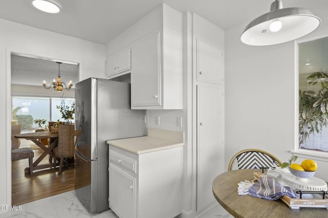 kitchen with stainless steel fridge, white cabinetry, pendant lighting, and an inviting chandelier