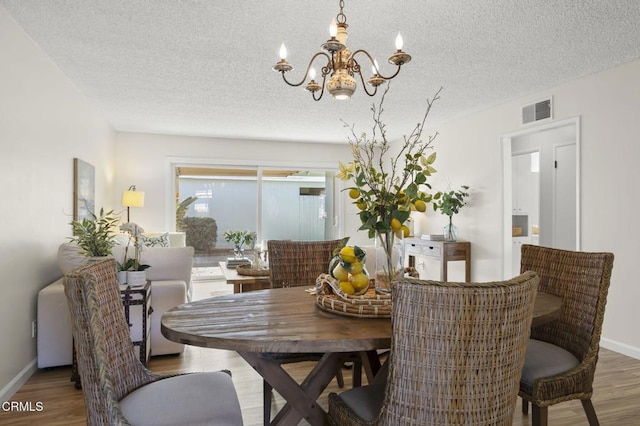 dining space with hardwood / wood-style flooring, a textured ceiling, and a notable chandelier