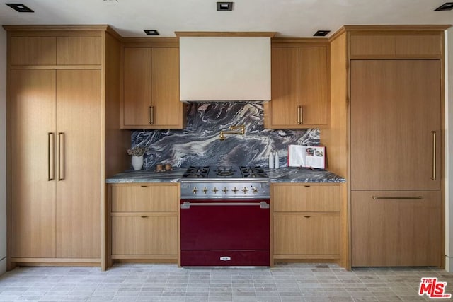 kitchen with backsplash, dark stone countertops, wall chimney range hood, and range