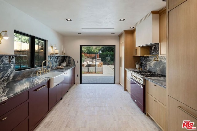 kitchen featuring backsplash, dark stone counters, sink, high end stainless steel range, and light brown cabinetry