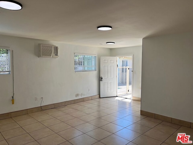 tiled empty room featuring an AC wall unit and a wealth of natural light