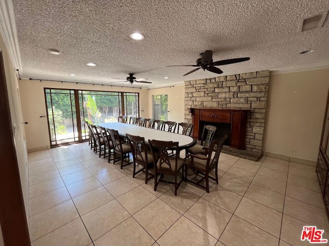 dining space with a stone fireplace, ceiling fan, light tile patterned floors, and a textured ceiling