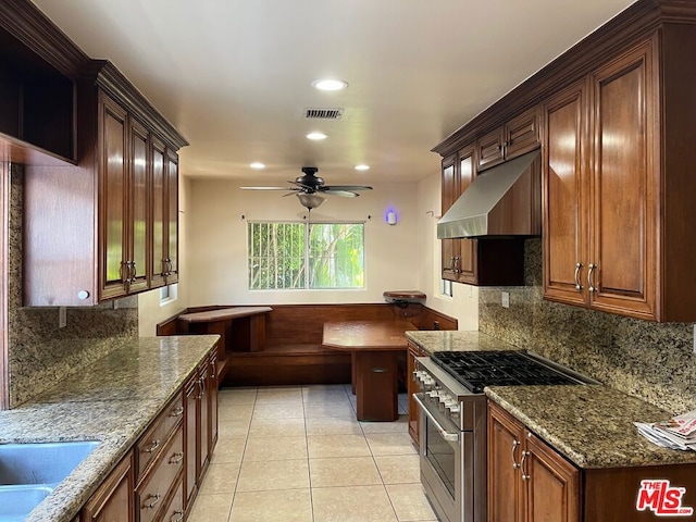 kitchen with ceiling fan, light tile patterned floors, dark stone counters, high end range, and exhaust hood