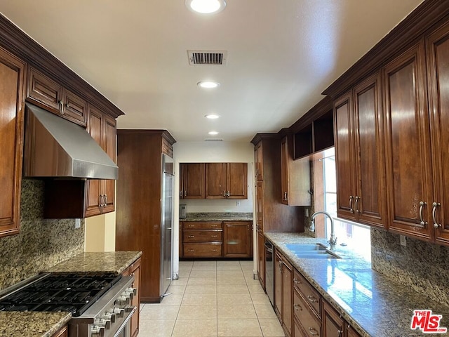 kitchen featuring sink, wall chimney range hood, light stone counters, stainless steel range oven, and light tile patterned flooring