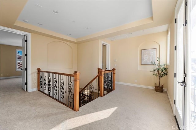 hallway featuring a tray ceiling and light colored carpet