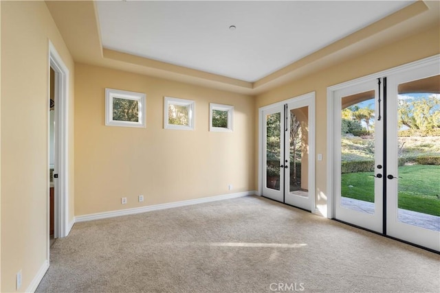 unfurnished room with a raised ceiling, light carpet, and french doors