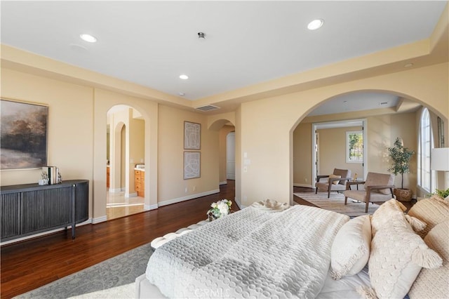 bedroom featuring a tray ceiling, ensuite bathroom, and hardwood / wood-style flooring