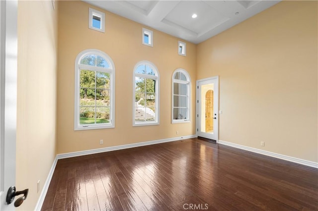 unfurnished room with beam ceiling, dark hardwood / wood-style flooring, a high ceiling, and coffered ceiling