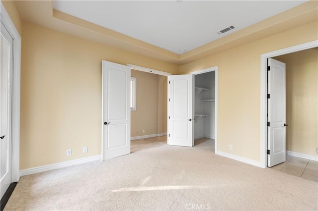 unfurnished bedroom featuring light carpet, a walk in closet, a tray ceiling, and a closet