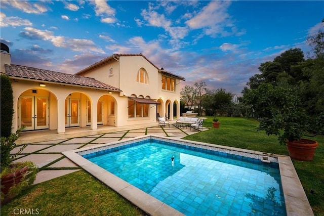 back house at dusk with french doors, a yard, and a patio area