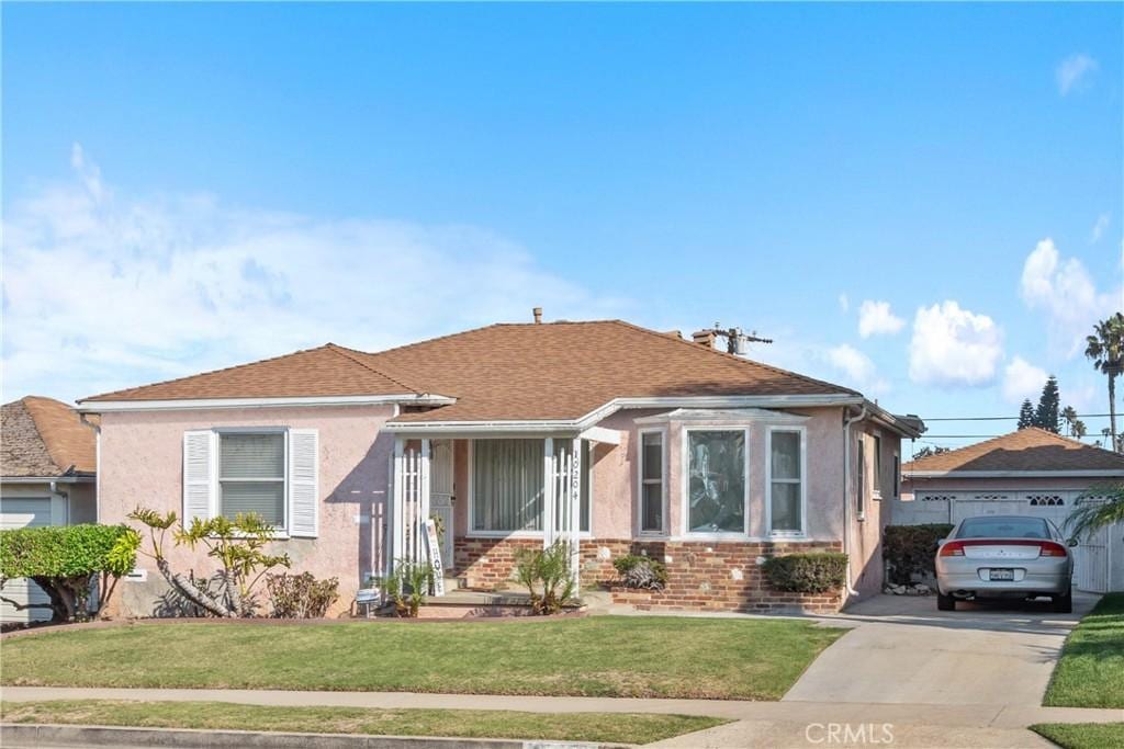 view of front of home with brick siding, roof with shingles, a front yard, and stucco siding